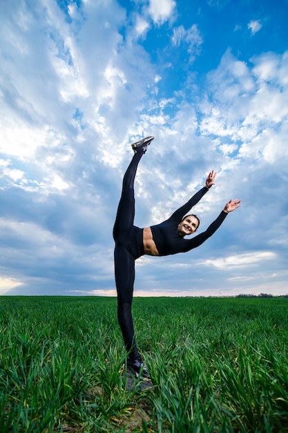 Schönes Mädchenmodell auf grünem Gras tun Yoga. Eine schöne Brünette auf einem grünen Rasen führt akrobatische Elemente durch. flexible Turnerin in schwarz macht Übungen