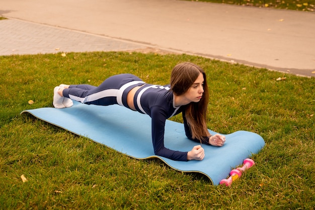 Schönes Mädchentraining. Sportliches Mädchen in einer Sportbekleidung. Mädchen, das Übungsplanke auf der Matte im Park tut