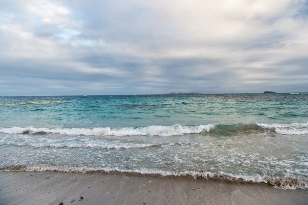 Schönes marineblaues Meer auf bewölktem Himmelshintergrund Meereswellen am Sandstrand Meeresküste