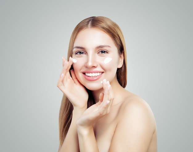 Schönes Model-Mädchen, das eine kosmetische Creme auf ihr Gesicht auf weißes Porträt einer gesunden Frau aufträgt
