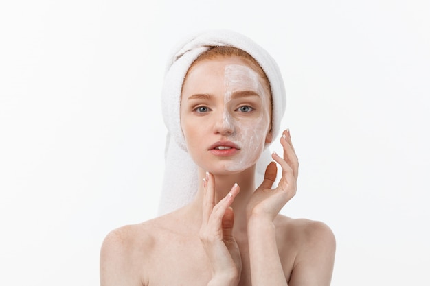 schönes Modell, das kosmetische Sahnebehandlung auf ihrem Gesicht auf Weiß aufträgt.