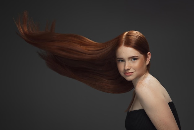 Schönes Modell mit langen glatten, fliegenden roten Haaren einzeln auf dunklem Studiohintergrund.