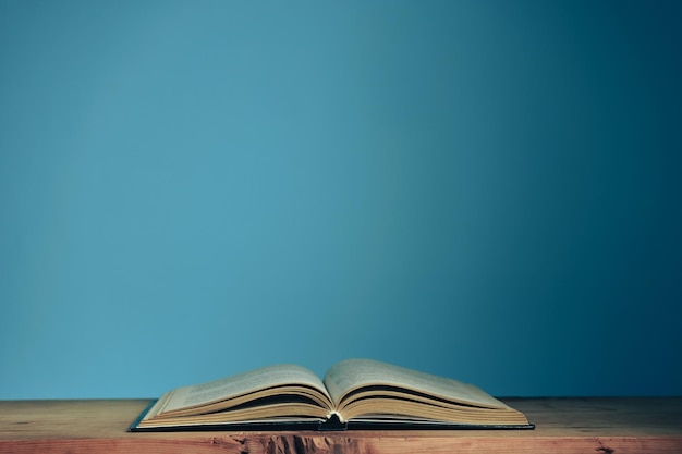 Schönes offenes Buch auf einem roten Holztisch und blauem Wandhintergrund