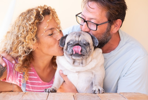 Schönes Paar, das ihren alten Mops umarmt und küsst. Schöne Familie und beste Freunde Konzept