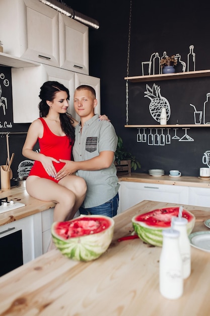 Schönes Paar erwartet kleines Baby Fürsorglicher Ehemann küsst schöne schwangere Frau beim Kochen in der Küche Zukünftige Eltern berühren den Bauch und umarmen sich Konzept der Schwangerschaft