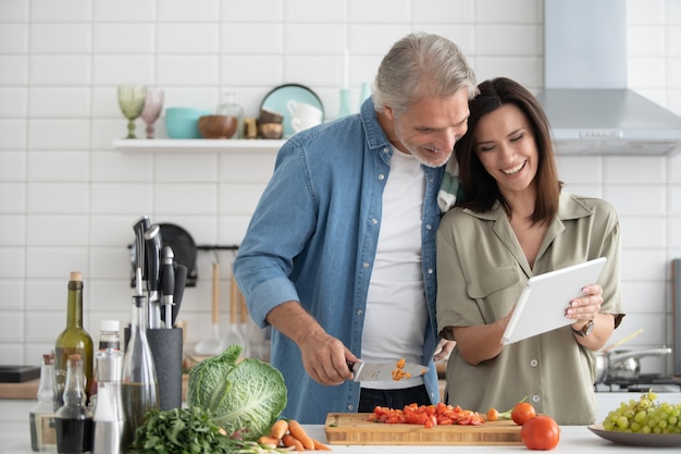 Schönes Paar mit einem digitalen Tablet und lächelnd beim Kochen in der Küche zu Hause