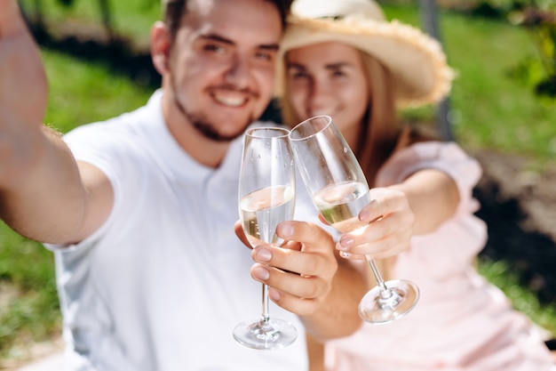 Schönes Paar sitzt auf dem Plaid, das Gläser Wein hält und selfies macht.