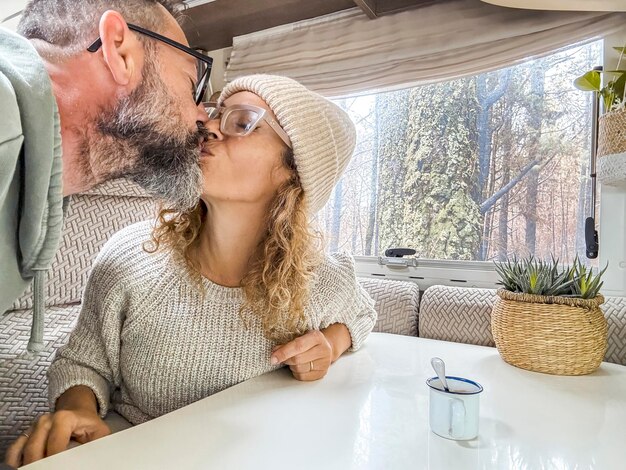 Schönes Paar tauscht sich in einem Wohnwagen Küsse aus, macht Fotos mit ihren Handys und lächelt. Ehemann und Frau genießen ihren Urlaub im Wald glücklich.