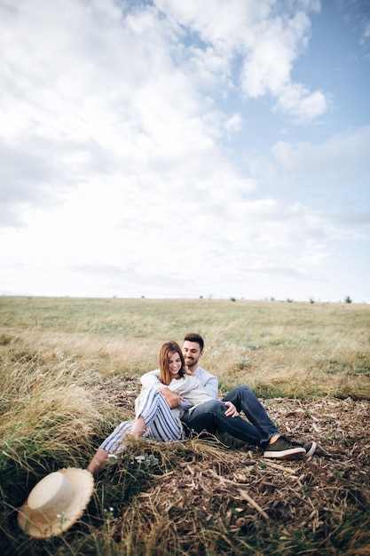 Schönes Paar umarmt, küsst und lächelt gegen den Himmel, der auf Gras sitzt. Platz für Text