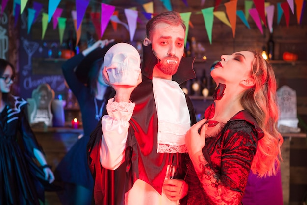 Schönes Paar verkleidet wie Dracula und eine sexy Hexe für die Halloween-Party. Dracula hält einen gruseligen Schädel.