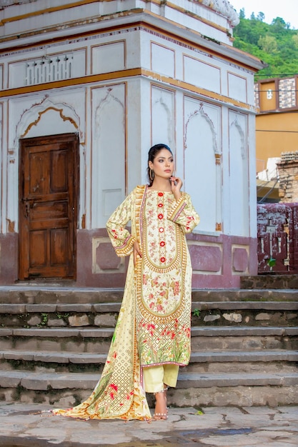 Schönes pakistanisches Mädchen posiert auf Treppen in traditionellem Designerkleid für Fotoshootings