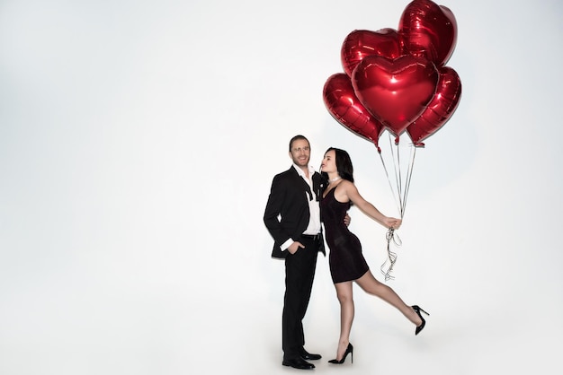 Schönes positives Paar hält rote herzförmige Ballons am Valentinstag auf weiß