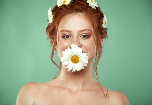 Schönes positives redheaded Mädchen mit einer Kamillenkrone auf ihrem Kopf