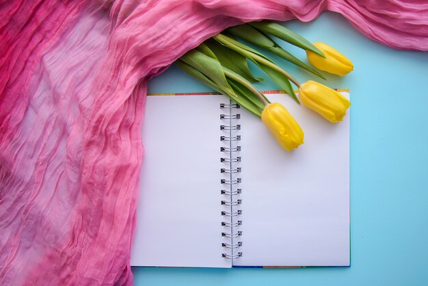 Schönes romantisches Bild mit Notizblock, Tee und Tulpen auf blauem Hintergrund