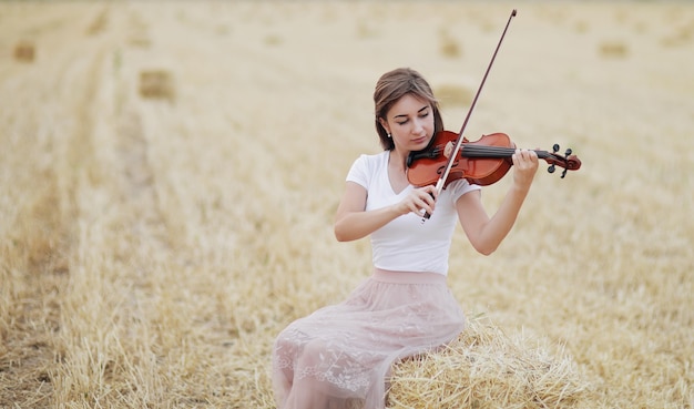 Schönes romantisches Mädchen mit losen Haaren, die die Geige im Feld spielen.