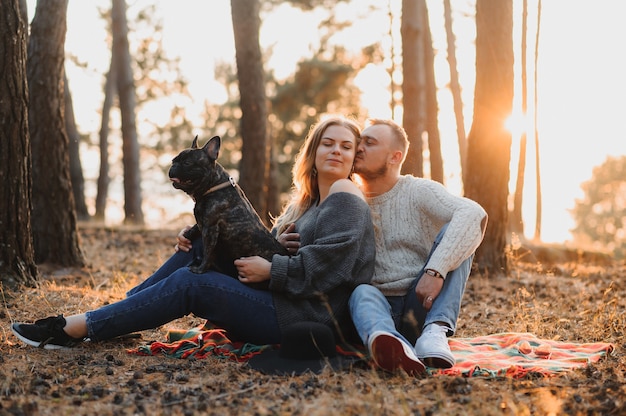 Schönes romantisches Paar hat Spaß mit ihrer französischen Bulldogge des Hundes draußen im Herbstwald bei Sonnenuntergang