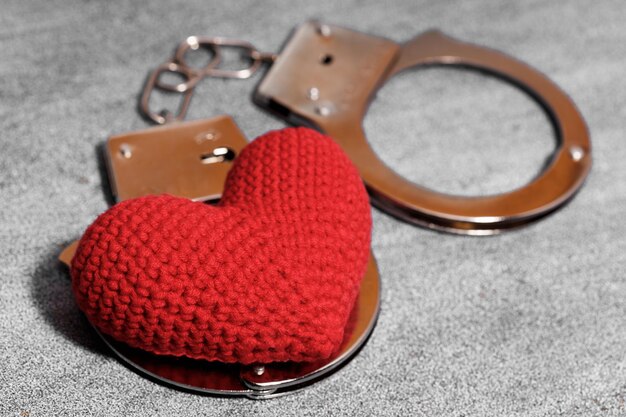 Schönes rotes Herz mit Handschellen liegt auf einem grauen Steinhintergrund. Foto in hoher Qualität