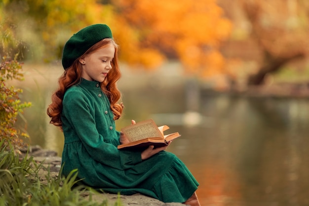 Schönes rothaariges Mädchen in einem grünen Kleid und im Herbst mit einem Buch im Park spazieren gehen