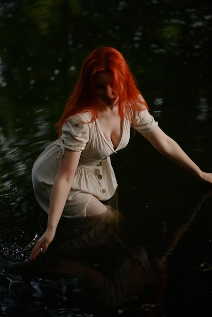 Schönes rothaariges Mädchen in einem weißen Kleid im See