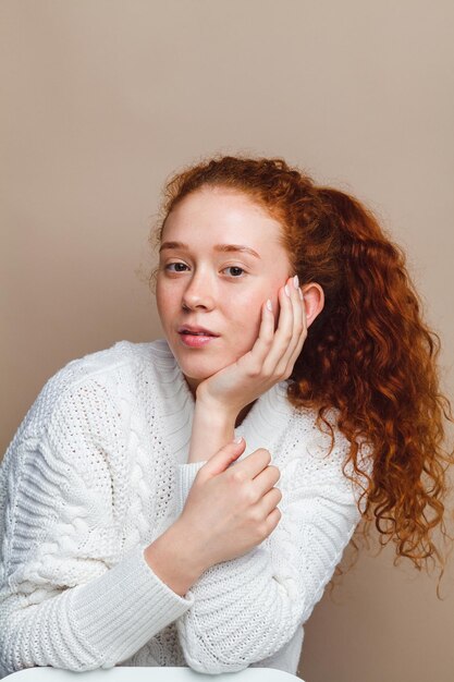 Schönes rothaariges Mädchen in einem weißen Strickpullover auf beigem Hintergrund. Keine Retusche, kein Make-up