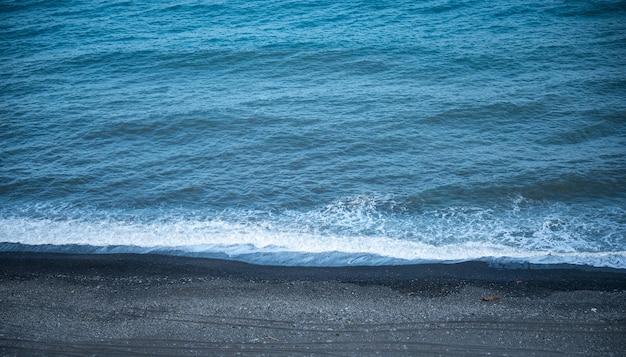 Schönes ruhiges und friedliches Wasser, das tagsüber mit Wellen in Richtung Strand mit grünen hohen Bäumen gegen bewölkten blauen Himmel fließt, ohne dass Menschen in der Nähe sind