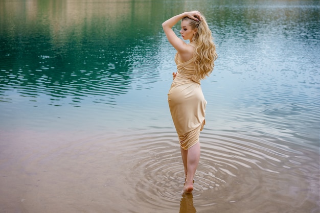 Schönes schlankes Mädchen mit dem langen Haar, das im Wasser stehend aufwirft.