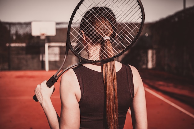 Schönes, schlankes Mädchen mit einem Tennisschläger steht mit dem Rücken auf dem Tennisplatz