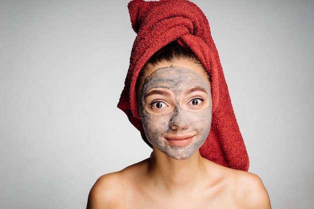 Schönes schönes Mädchen mit einem roten Handtuch auf dem Kopf hat eine nützliche Maske auf ihr Gesicht gelegt, Day Spa