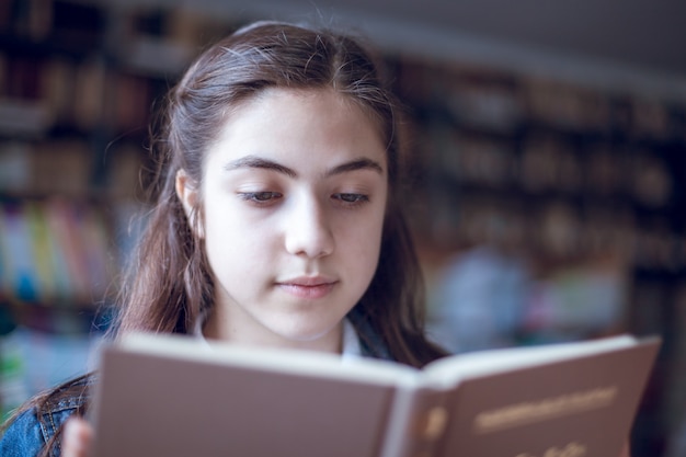 Schönes Schulmädchen in der Bibliothek, die ein Buch liest, Bildung