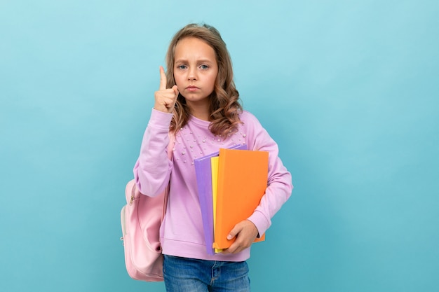 Schönes Schulmädchen in der lila Bluse denkt über das Studieren isoliert auf blauem Hintergrund nach