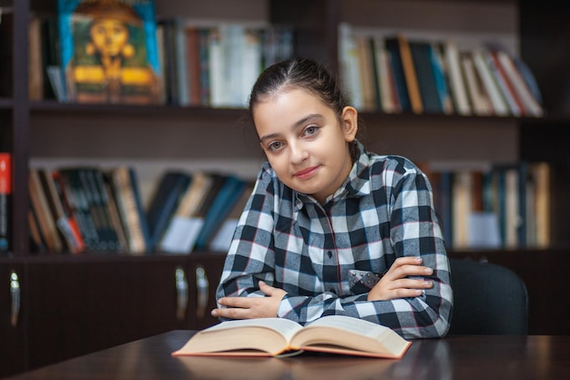 Foto schönes schulmädchen sitzt in der bibliothek und liest ein buch