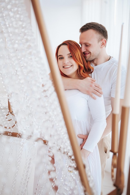 Schönes schwangeres Mädchen im weißen Kleid mit Ehemann im Studio