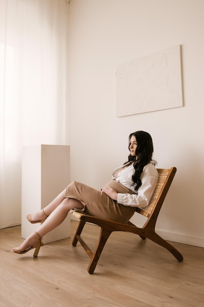 Schönes schwangeres Mädchen mit Locken in einem Kleid in einem hellen Studio mit stilvollem Interieur das Konzept einer glücklichen Schwangerschaft und Familie