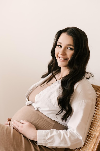 Schönes schwangeres Mädchen mit Locken in einem Kleid in einem hellen Studio mit stilvollem Interieur das Konzept einer glücklichen Schwangerschaft und Familie