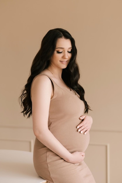 Foto schönes schwangeres mädchen mit locken in einem kleid in einem hellen studio mit stilvollem interieur das konzept einer glücklichen schwangerschaft und familie