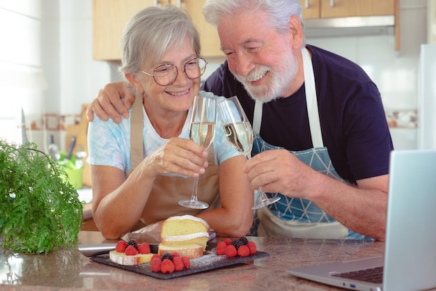 Schönes Seniorenpaar in der heimischen Küche, das sich seinen hausgemachten Pflaumenkuchen anschaut, der bereit ist, mit zwei Gläsern Wein zu toasten Kochen zu Hause für das Familienkonzept