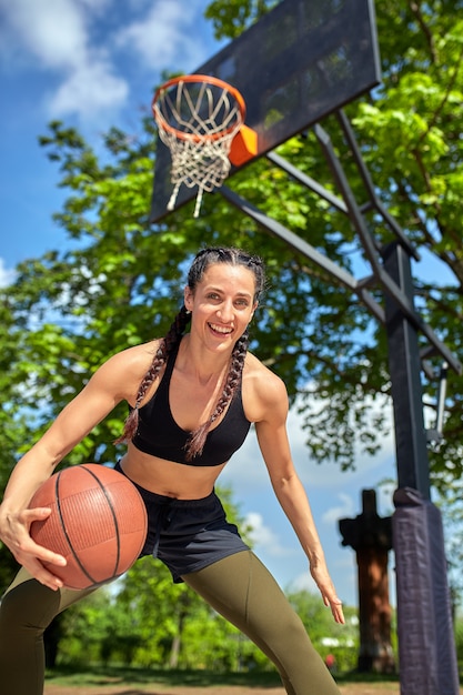 Schönes sexy Fitnessmädchen in schwarzer Sportkleidung mit perfektem Körper mit Basketball am Basketballplatz. Sport-, Fitness-, Lifestyle-Konzept