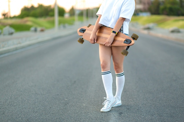 Schönes sexy junges Mädchen in kurzen Hosen gehend mit longboard im sonnigen Wetter. Freizeit. Gesunder Lebensstil. Extremsportarten. Modeblick, Hippie-Porträt im Freien, Bali, Turnschuhe, Hippie, sunse