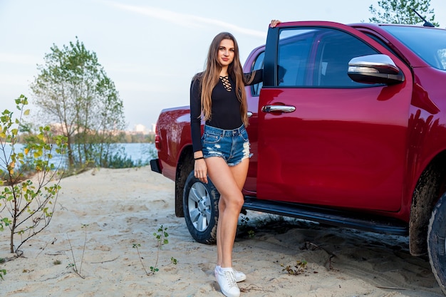 Schönes sexy Mädchen mit langen Haaren in kurzen Jeans-Shorts und einer Pose in der Nähe einer roten Spitzhacke