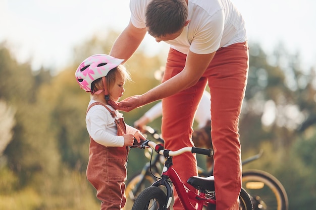 Schönes Sonnenlicht Vater im weißen Hemd, der seiner Tochter beibringt, wie man im Freien Fahrrad fährt