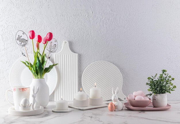 Schönes Stillleben für die Osterfeiertage, weißes Geschirr, eine Vase mit Tulpen, bemalte Eier, Osterkerzen und Hasen, festlicher Hintergrund in der Küche