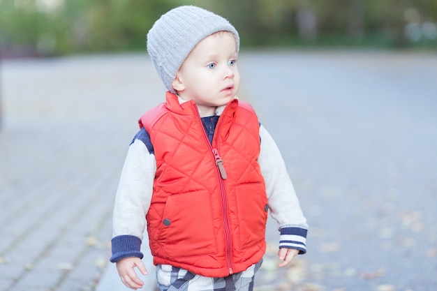 Schönes stilvolles Baby 2 Jahre alt, das in gefallene Blätter geht - Herbstszene. Kleinkind hat Spaß im Freien im herbstgelben Park