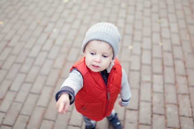 Schönes stilvolles Baby 2 Jahre alt, das in gefallene Blätter geht - Herbstszene. Kleinkind hat Spaß im Freien im herbstgelben Park