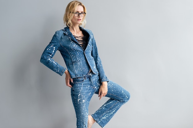 Schönes stilvolles blondes Modell im Jeansanzug posiert
