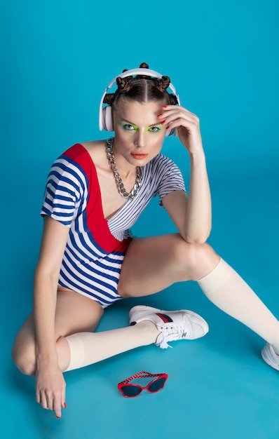 Foto schönes stilvolles weibliches modell mit hellem make-up, das musik auf blauem hintergrund im studio hört