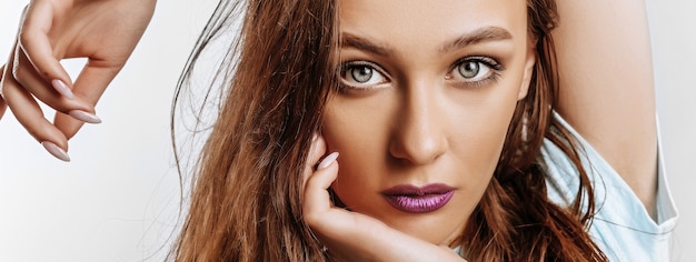 Schönes süßes brünettes Mädchen mit langen Haaren mit Mode-Make-up mit lila Lippen auf lokalisiertem Grau