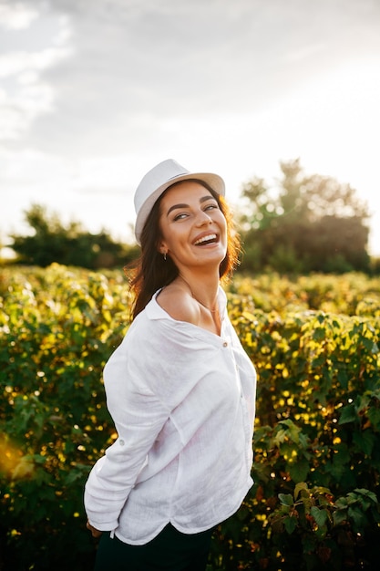 Schönes süßes sexy Mädchen in einem weißen Kleid, das auf einem Feld von Sonnenblumen spazieren geht und ein schönes Lächeln lächelt