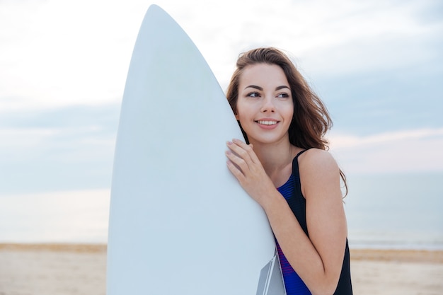 Schönes Surfer-Teenager-Mädchen, das mit Surfbrett am Strand steht