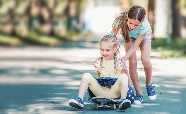 Schönes Teenager-Mädchen, das am sonnigen Sommertag ihre kleine blonde Schwester auf Skateboard im Park reitet