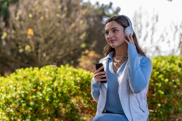 Foto schönes teenager-mädchen, das nachmittags mit ihrem handy in einem park musik hört